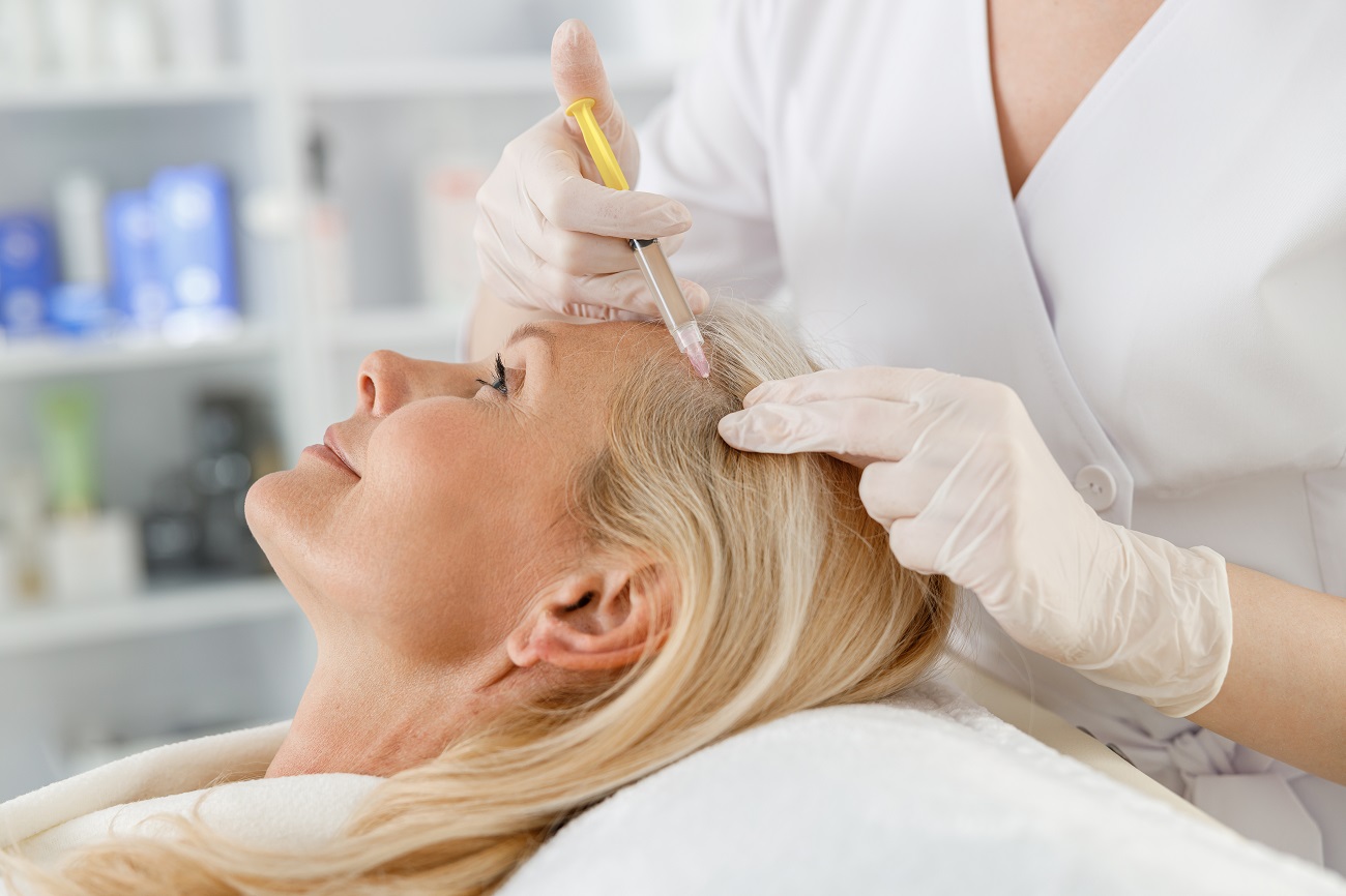 cosmetologist does prp therapy against hair loss of a senior blond woman in a beauty salon